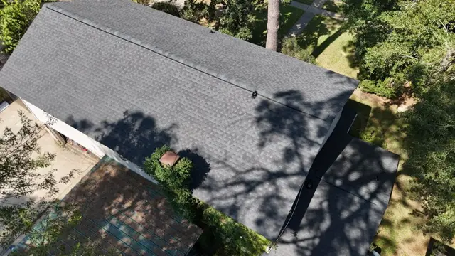 A close aerial view of the new shingle field and ridge on the Cypress roof, with tree shadows falling across the slope. Uniform color and tight shingle lines are what a properly installed roof should look like from above.