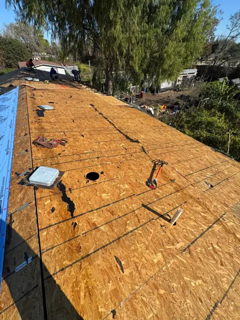 Roof replacement in progress in Pearland, TX: new OSB roof decking installed after the old shingles and water-damaged boards were torn off. Replacing soft or rotted decking gives the new shingles a solid surface to nail into, which matters for wind resistance. Openings for roof vents are already cut, and synthetic underlayment is starting along one edge.