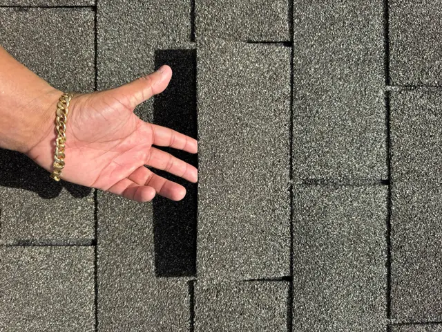 An unsealed shingle lifted to expose the open seam and bare seal line underneath it. When this pattern repeats across many tabs on several slopes, it points to storm-wide wind damage rather than normal aging, which matters for whether an insurance company approves repair or full replacement. Cloud IX photographs each damaged tab with a hand for scale so the homeowner and the adjuster can see exactly what was found.