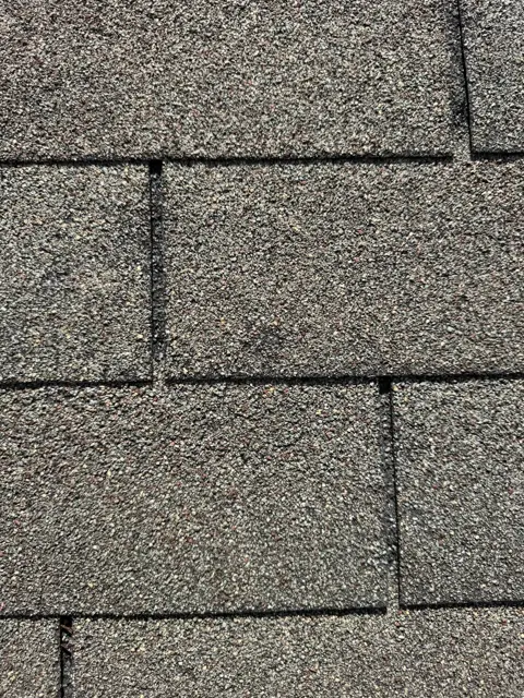 Detailed close-up of the shingle surface showing granule loss and gaps at the tab joints, recorded during the full-roof inspection for the insurance file. Granules protect the asphalt from UV and heat, and storm impacts or wind scouring can strip them away, shortening the roof's life. Close-up photos like this give adjusters and homeowners a clear, dated record of the roof's condition at the time of the storm.