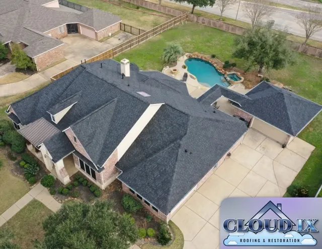 Front-corner aerial of the finished roof showing the dormer, the standing-seam metal porch roof, the attached garage wing and the driveway cleaned up after the job. A full reroof from the decking up with impact-rated shingles is a strong way to protect a home in hail country. In Texas, insurance premium discounts are usually tied to Class 4 shingles, so homeowners choosing between Class 3 and Class 4 should ask their agent what their policy rewards.